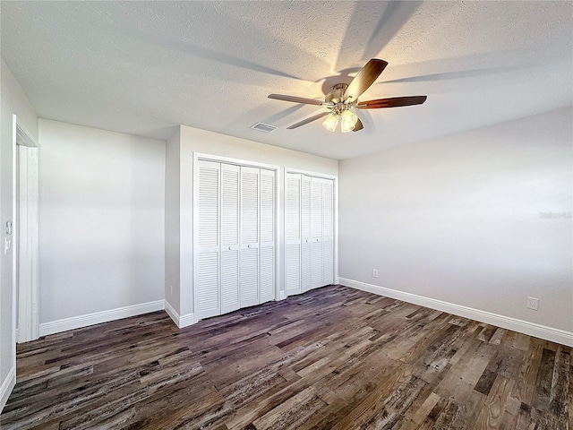 unfurnished bedroom featuring multiple closets, ceiling fan, dark hardwood / wood-style flooring, and a textured ceiling