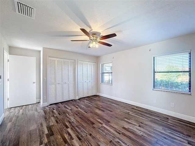 unfurnished bedroom with wood finished floors, baseboards, two closets, and a textured ceiling