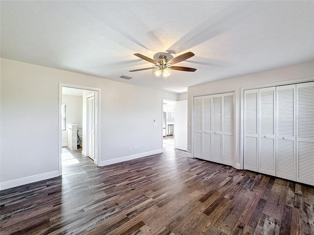 unfurnished bedroom with dark wood-style floors, multiple closets, baseboards, and a textured ceiling