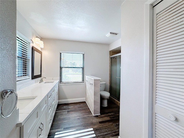 full bath with wood finished floors, toilet, a shower stall, double vanity, and baseboards