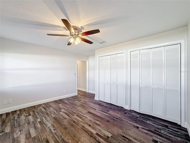 unfurnished bedroom with multiple closets, dark wood-type flooring, baseboards, a ceiling fan, and a textured ceiling