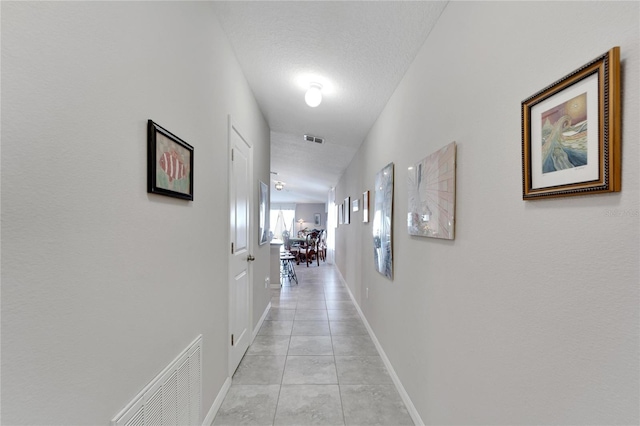 corridor with a textured ceiling, lofted ceiling, and light tile patterned flooring