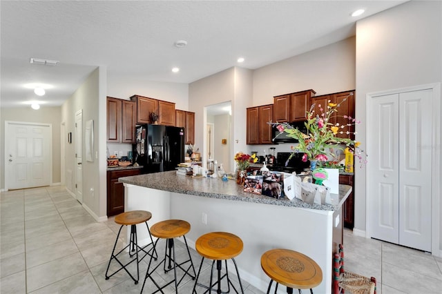 kitchen featuring a breakfast bar area, an island with sink, black appliances, and light tile patterned floors