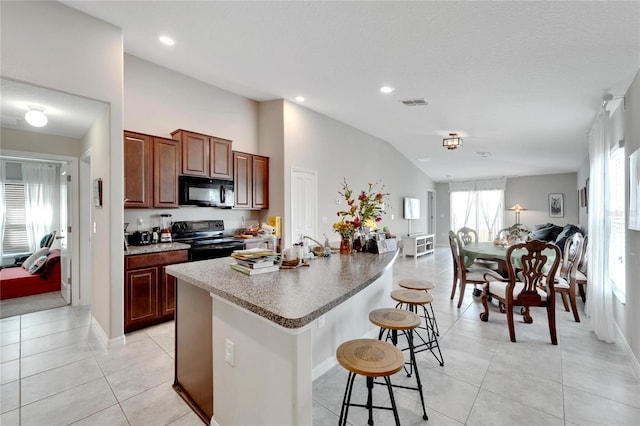 kitchen with vaulted ceiling, a kitchen island with sink, a breakfast bar, light tile patterned flooring, and black appliances