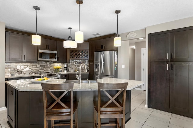 kitchen featuring tasteful backsplash, a center island with sink, dark brown cabinets, and appliances with stainless steel finishes