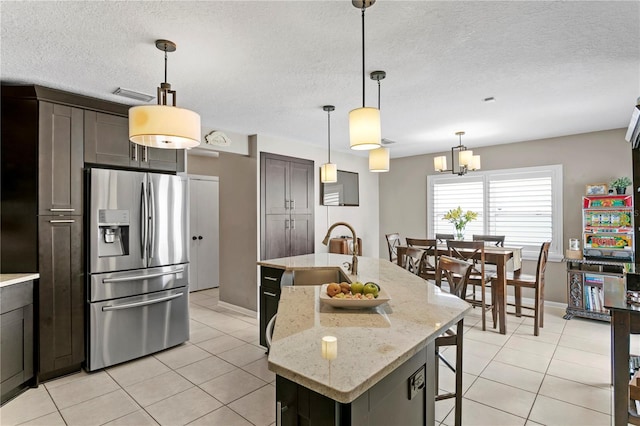 kitchen featuring sink, stainless steel fridge with ice dispenser, light stone counters, an island with sink, and dark brown cabinets