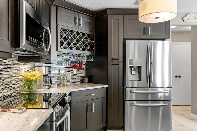 kitchen with light stone counters, dark brown cabinetry, stainless steel appliances, and tasteful backsplash