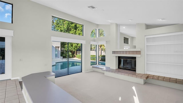 living room featuring a tile fireplace, built in features, a towering ceiling, and light colored carpet