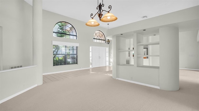 spare room with a towering ceiling, light carpet, and a chandelier