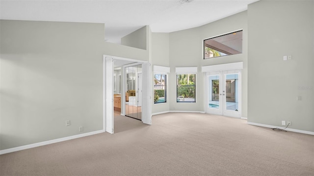 empty room with french doors, light colored carpet, and high vaulted ceiling