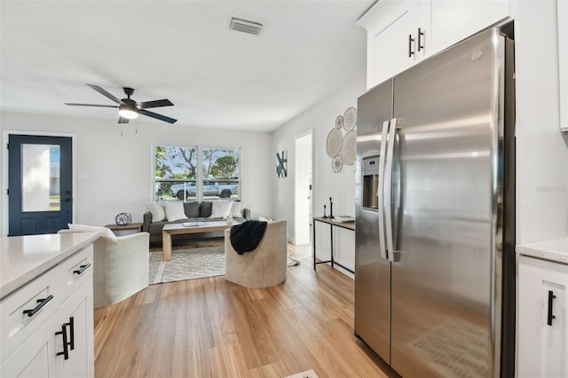 kitchen featuring light wood-type flooring, light stone counters, ceiling fan, stainless steel fridge with ice dispenser, and white cabinetry