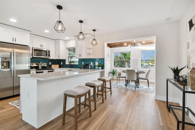 kitchen with hanging light fixtures, tasteful backsplash, light hardwood / wood-style flooring, white cabinets, and appliances with stainless steel finishes