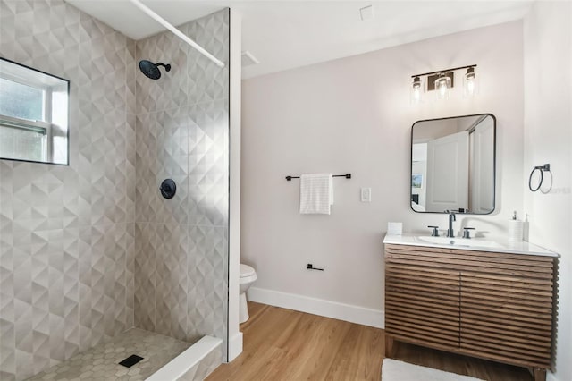 bathroom with a tile shower, vanity, hardwood / wood-style flooring, and toilet