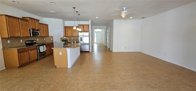 kitchen with ceiling fan, backsplash, an island with sink, pendant lighting, and appliances with stainless steel finishes