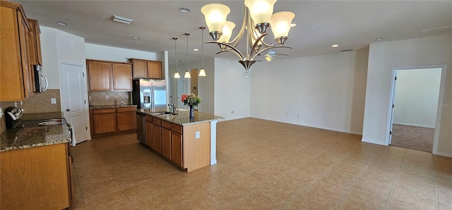 kitchen with stainless steel appliances, pendant lighting, a center island with sink, dark stone countertops, and a chandelier