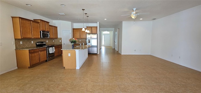 kitchen featuring backsplash, a kitchen island with sink, appliances with stainless steel finishes, decorative light fixtures, and light stone counters