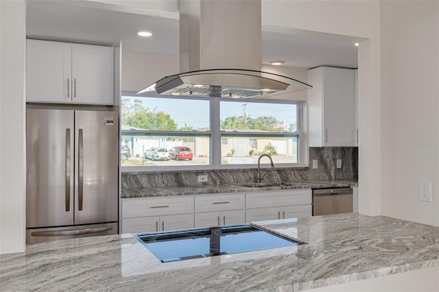 kitchen with white cabinets, sink, island range hood, appliances with stainless steel finishes, and light stone countertops