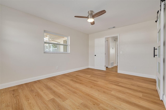 unfurnished room featuring a barn door, ceiling fan, and light hardwood / wood-style floors