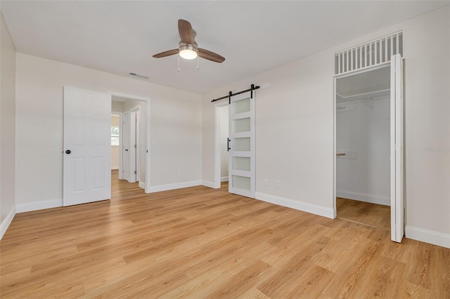 unfurnished bedroom featuring ceiling fan, a barn door, a spacious closet, light hardwood / wood-style floors, and a closet