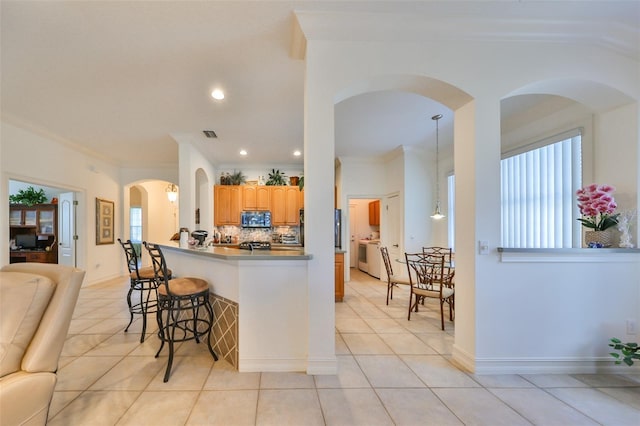1120 Emerald Dunes Dr, Sun City Center, FL 33573 - kitchen featuring stainless steel microwave, ornamental molding, a kitchen breakfast bar, tasteful backsplash, and light tile patterned flooring