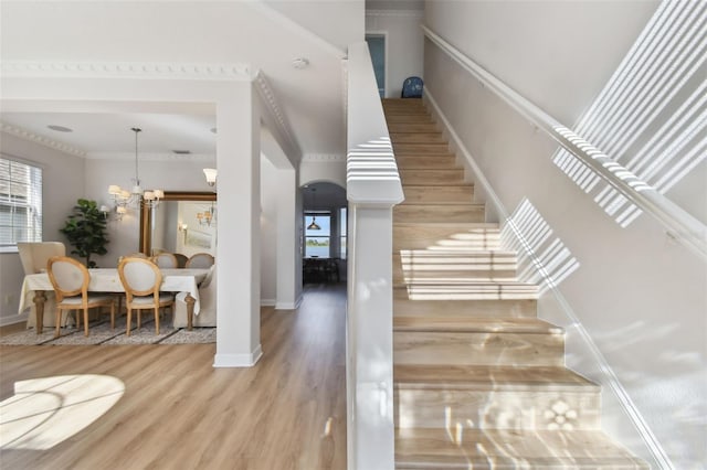 staircase featuring hardwood / wood-style flooring, crown molding, a healthy amount of sunlight, and a notable chandelier