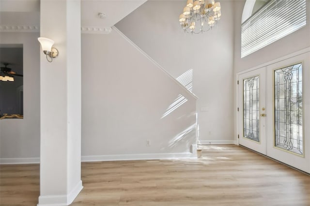 entrance foyer featuring crown molding, french doors, ceiling fan with notable chandelier, and light wood-type flooring