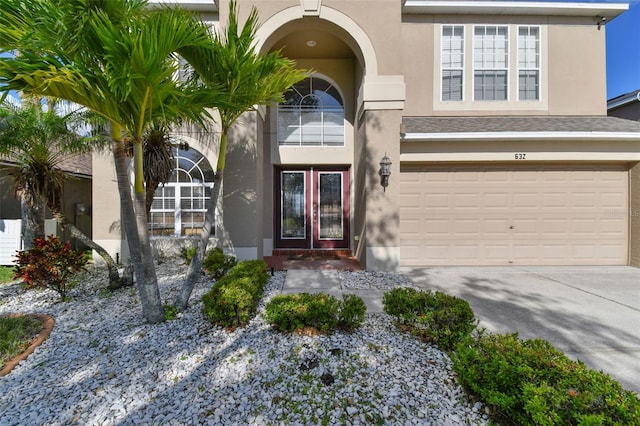 view of exterior entry with a garage, driveway, french doors, and stucco siding