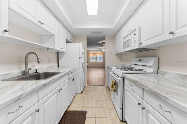 kitchen with white appliances, a raised ceiling, sink, light tile patterned floors, and white cabinetry