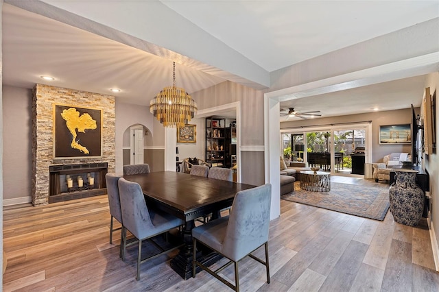 dining room featuring a fireplace, ceiling fan with notable chandelier, and light wood-type flooring