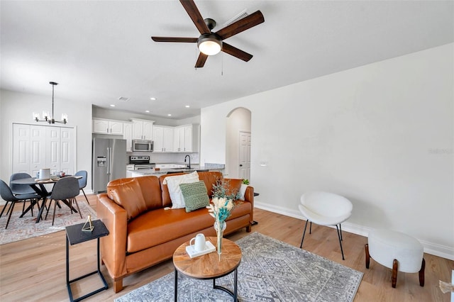 living room with light hardwood / wood-style flooring, ceiling fan with notable chandelier, and sink