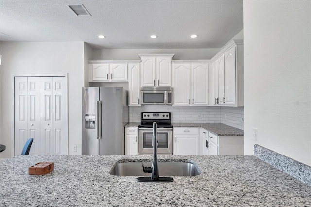 kitchen featuring backsplash, sink, light stone counters, white cabinetry, and stainless steel appliances