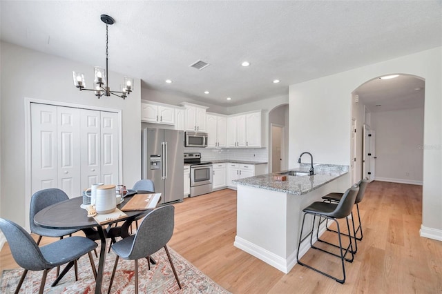 kitchen featuring kitchen peninsula, light wood-type flooring, stainless steel appliances, and white cabinetry