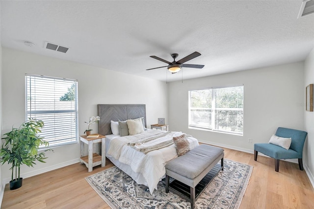 bedroom with ceiling fan, light wood-type flooring, a textured ceiling, and multiple windows