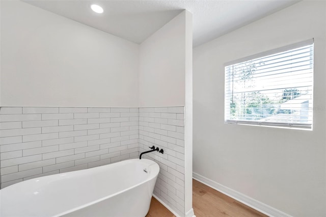 bathroom featuring hardwood / wood-style flooring, a bath, and tile walls