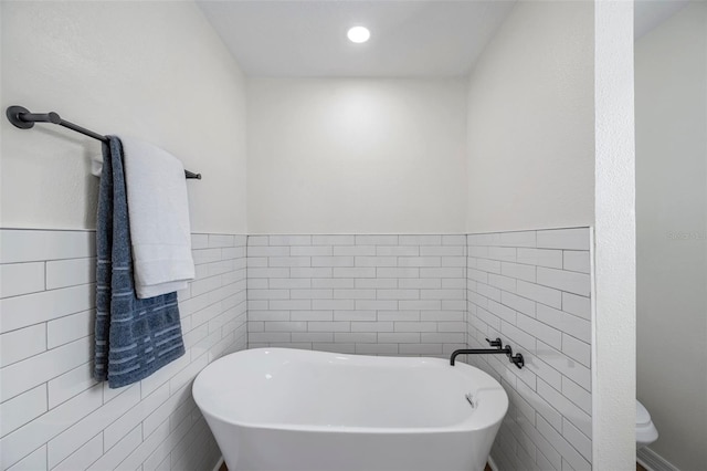 bathroom with a bath, tile walls, and toilet