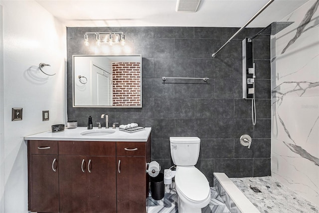 bathroom with a tile shower, vanity, tile walls, and toilet