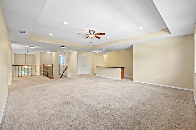 interior space featuring a tray ceiling, ceiling fan, light colored carpet, and a textured ceiling