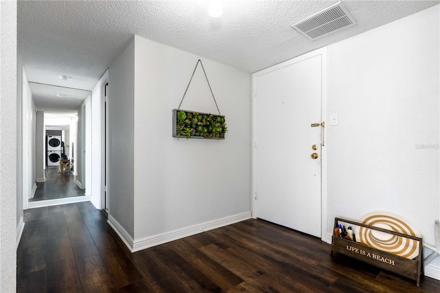 foyer entrance with dark wood-type flooring, stacked washing maching and dryer, and a textured ceiling