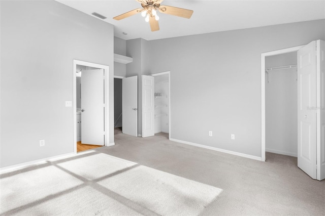 unfurnished bedroom with light carpet, a walk in closet, ceiling fan, connected bathroom, and a closet