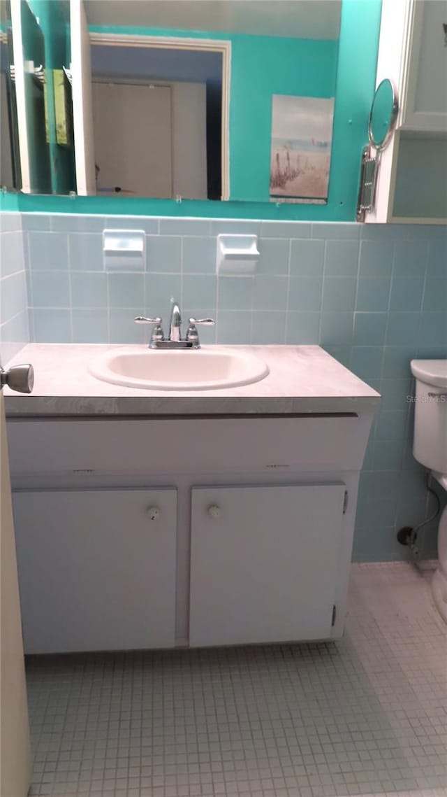 bathroom with toilet, vanity, tile walls, and tile patterned floors