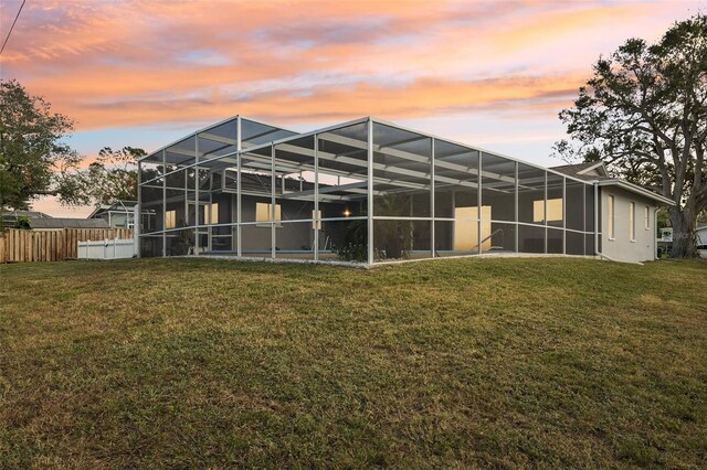 back house at dusk featuring a lanai and a yard