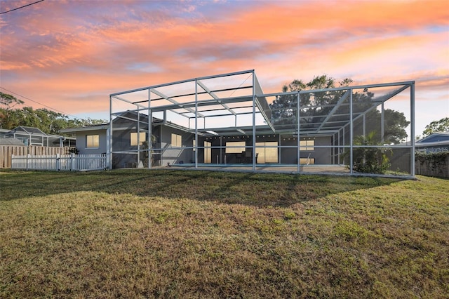 back house at dusk featuring a lawn and a lanai