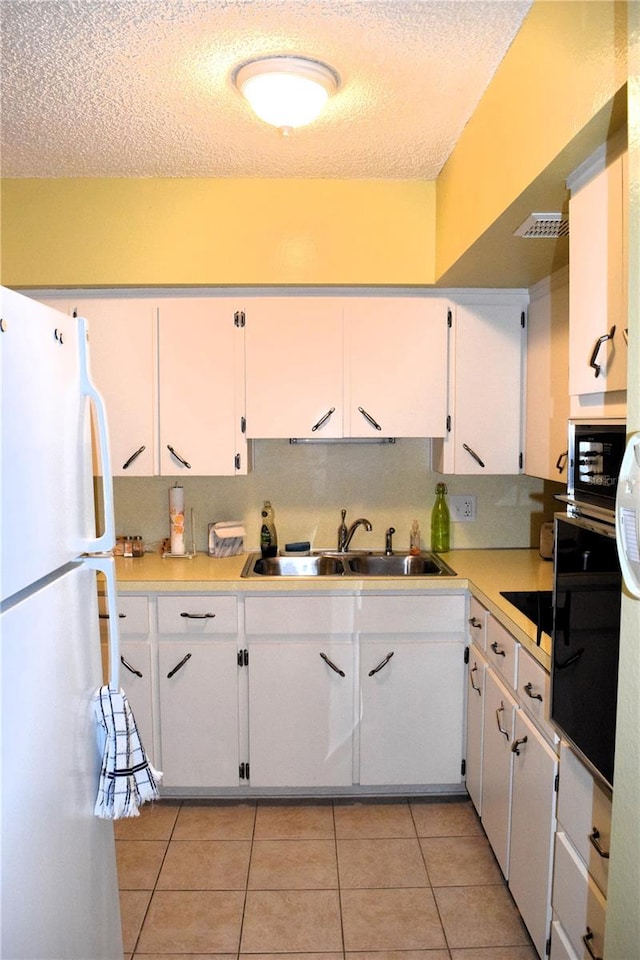 kitchen with a textured ceiling, sink, black appliances, light tile patterned floors, and white cabinets