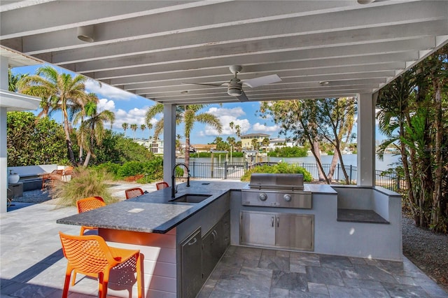 view of patio featuring ceiling fan, exterior kitchen, area for grilling, a water view, and a wet bar