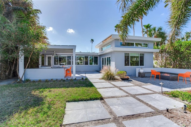 rear view of property with a lawn, ceiling fan, a fire pit, an outdoor bar, and a patio area