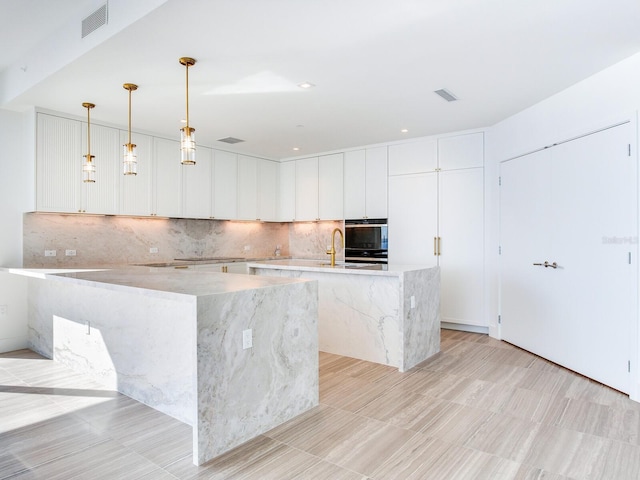 kitchen with decorative light fixtures, white cabinetry, a large island, and light stone counters