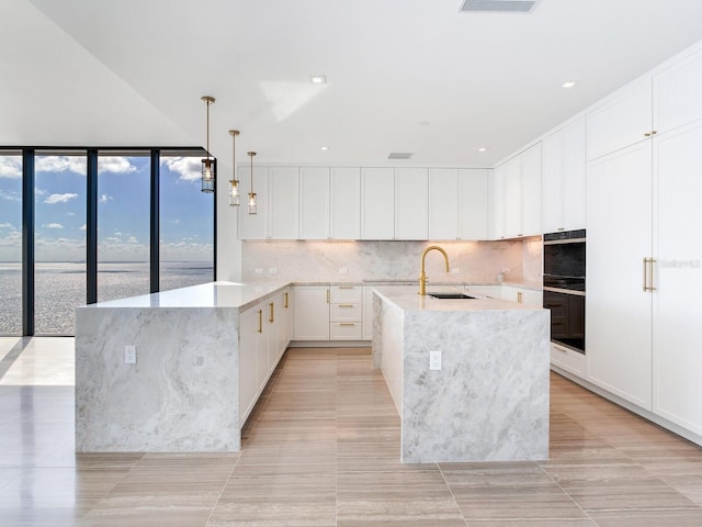 kitchen featuring white cabinets, a water view, double oven, and an island with sink