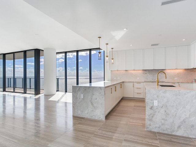 kitchen featuring white cabinets, decorative light fixtures, expansive windows, and sink