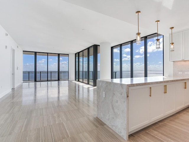 kitchen with white cabinetry, a water view, decorative light fixtures, expansive windows, and light stone countertops