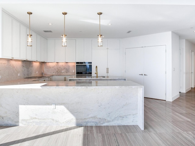 kitchen featuring light stone countertops, stainless steel double oven, sink, white cabinetry, and hanging light fixtures